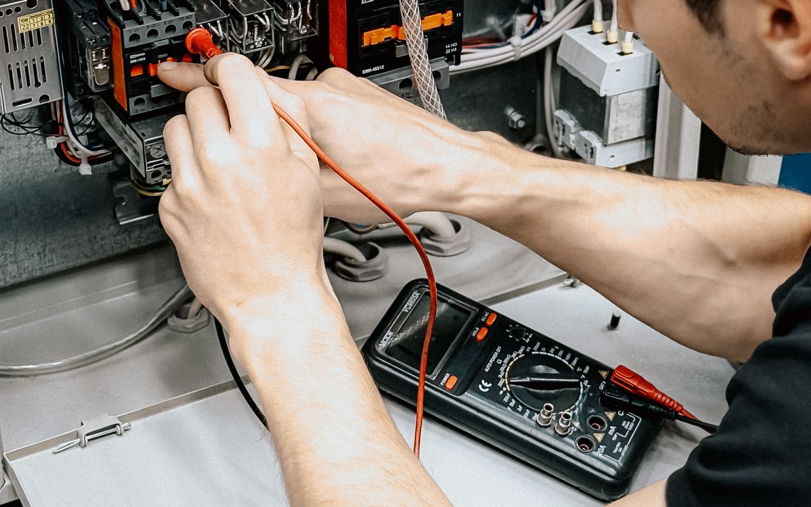Technician testing an open commercial electrical panel with a multimeter