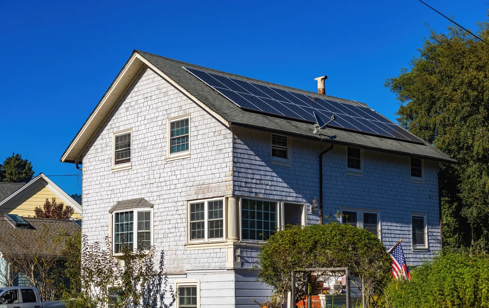 White two-story home with rooftop solar panels under a clear blue sky