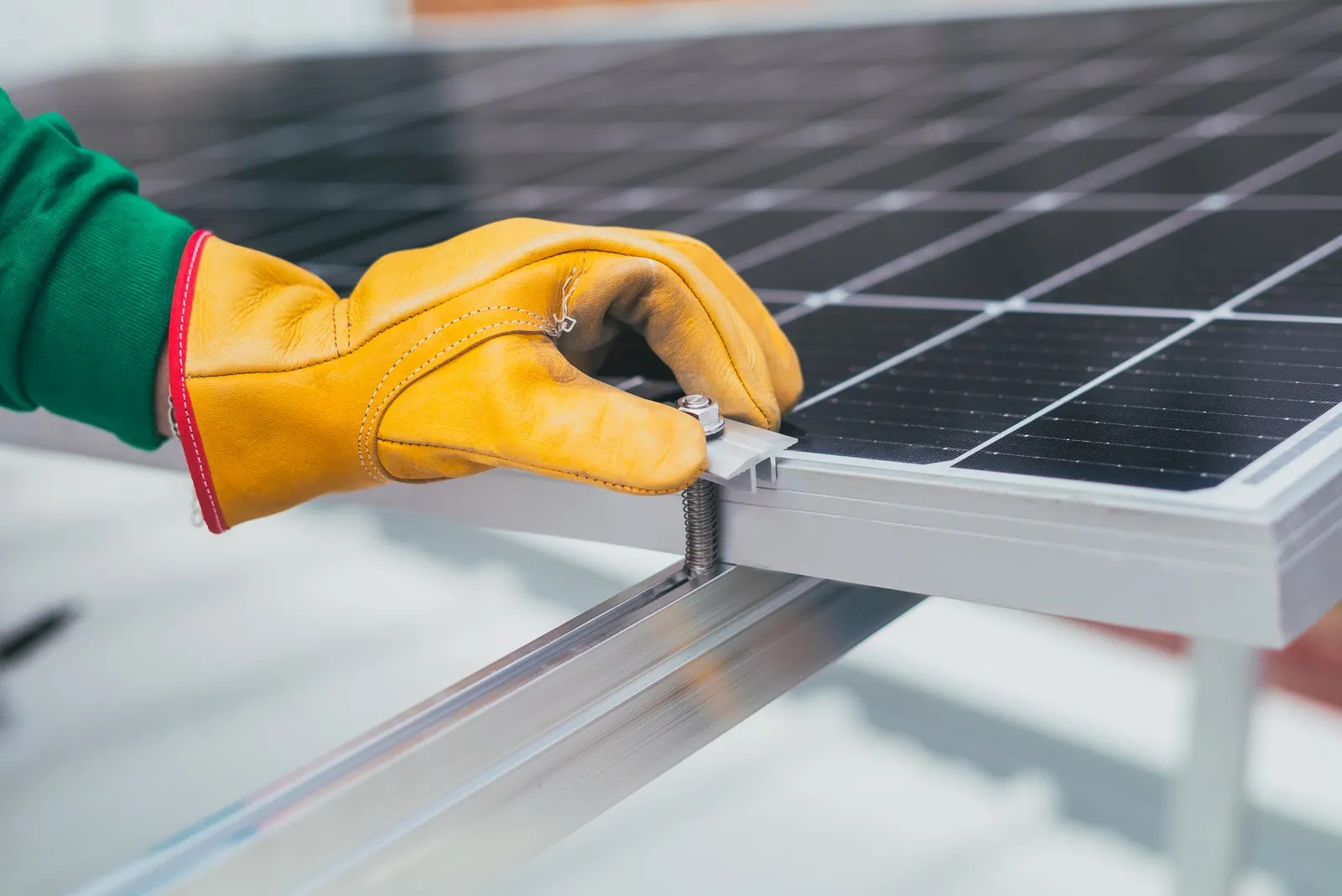 Gloved hand securing a mounting clamp on a solar panel frame