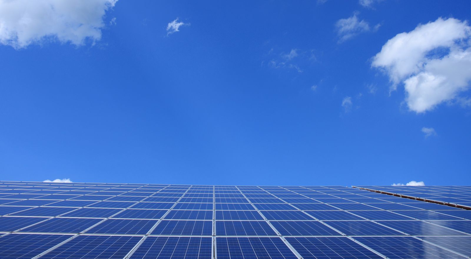 Solar panel array under a bright blue sky with clouds