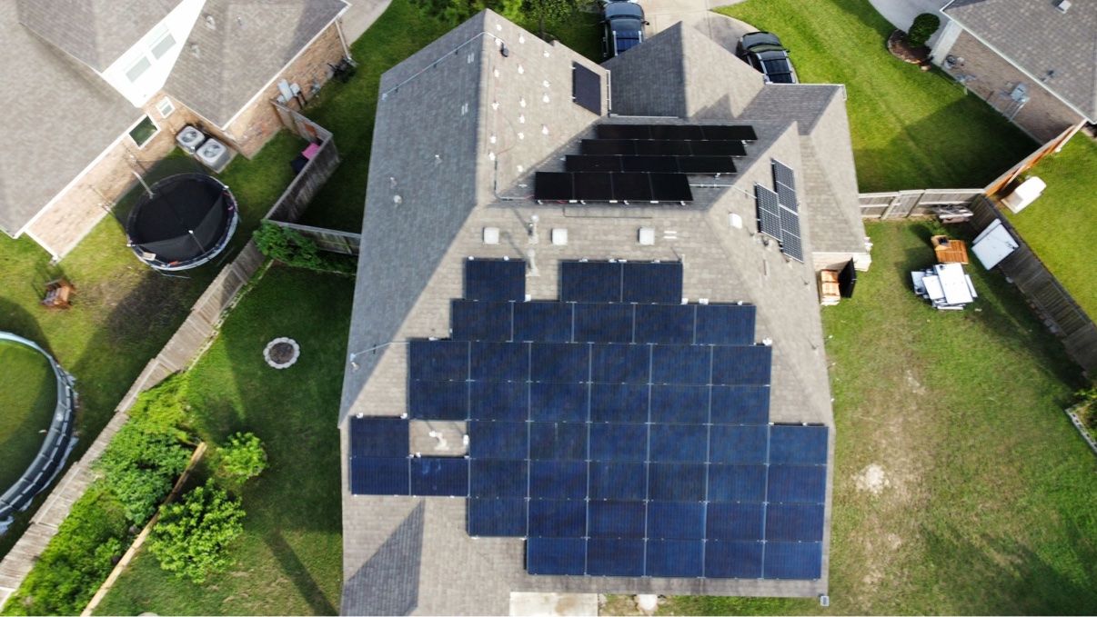 Aerial view of a large solar array on a roof above a fenced backyard