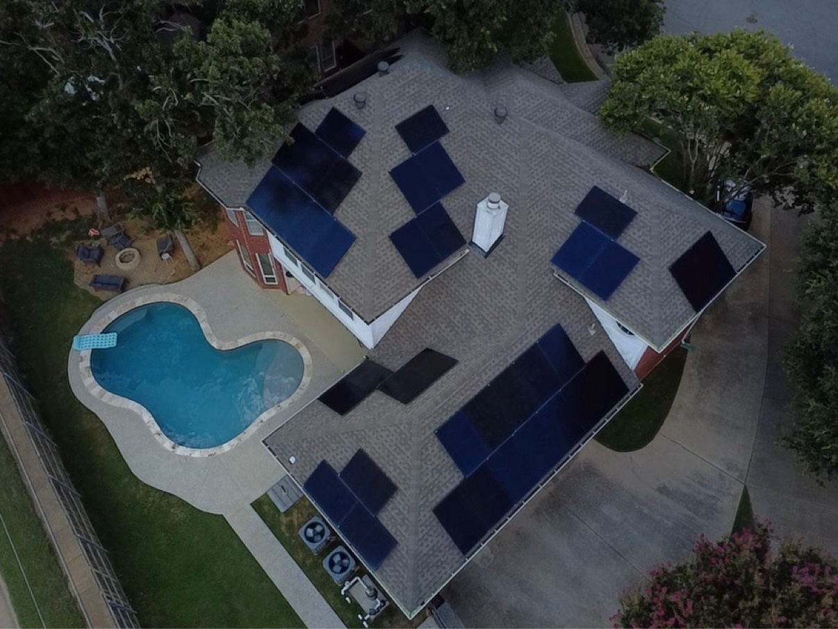 Aerial view at dusk of rooftop solar arrays on a home with a swimming pool